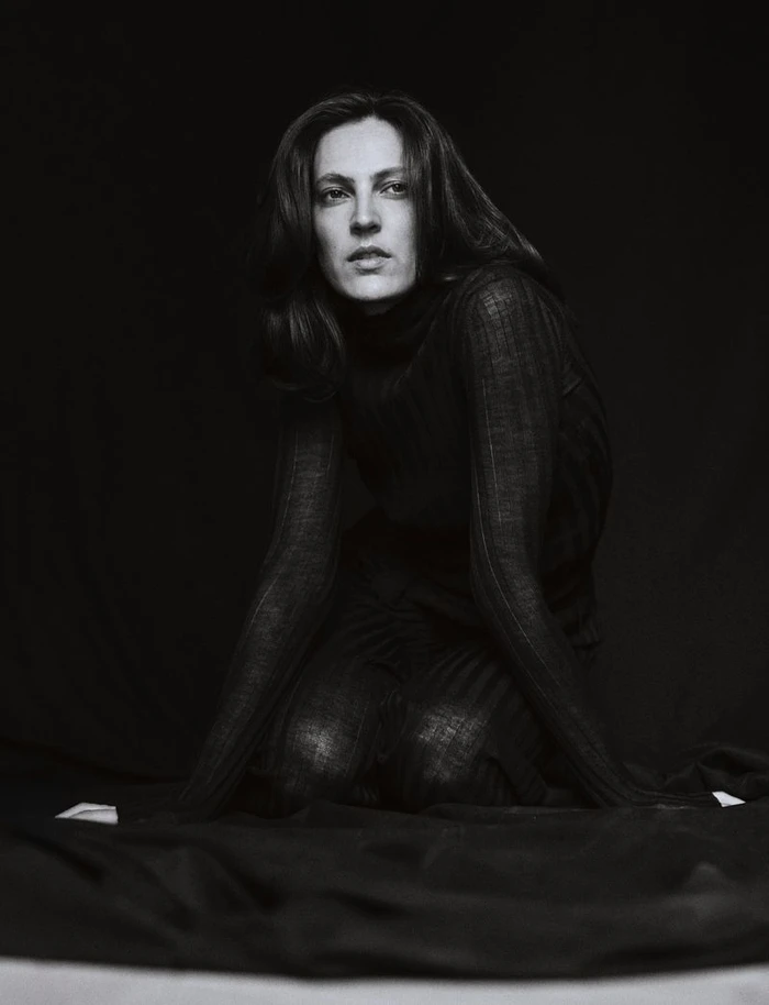 Model Othilia Simon kneeling in a dark textured top against a plain dark background for Numero Netherlands.