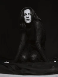 Model Othilia Simon kneeling in a dark textured top against a plain dark background for Numero Netherlands.