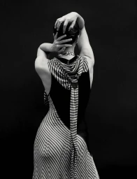 Model seen from behind with hands on head wearing a striped dress against a dark background for Numero Netherlands.