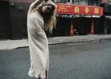 Model Felice Nova Noordhoff posing in a cream slip dress on an asphalt street in front of a red storefront.