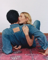 Dree Hemingway embraces Nick Delli Santi wearing a JW Anderson denim shirt on a patterned magenta rug.