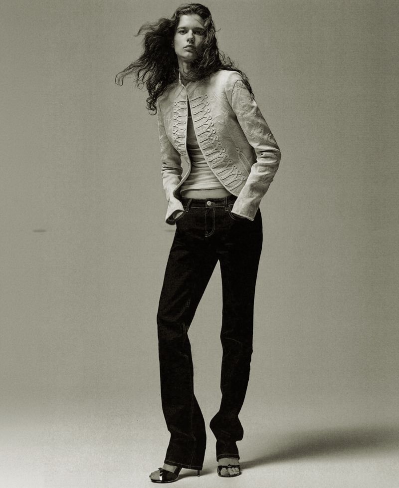 Model Felice Nova Noordhoff wearing a cream embroidered jacket and dark denim jeans standing against a grey studio backdrop.