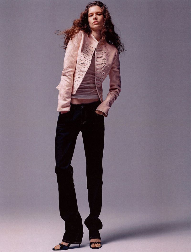 Model Felice Nova Noordhoff wearing a blush military jacket and dark denim jeans against a grey studio backdrop.