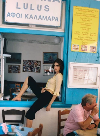 Model Zoi Mantzakanis lounges in a blue taverna windowsill wearing a yellow ruffled top and black capri pants.