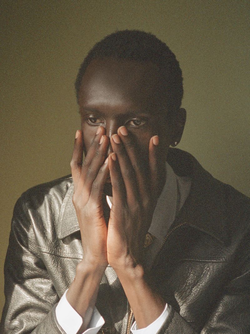 Model Daniel Ajang resting hands over his face wearing a black leather jacket against a muted background.