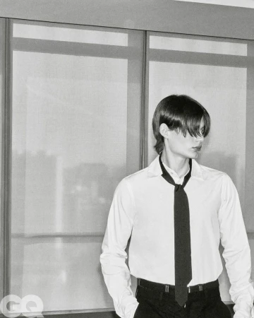 Model Meng Yu Qi in a white collared shirt and loose black tie standing in front of large paneled windows.