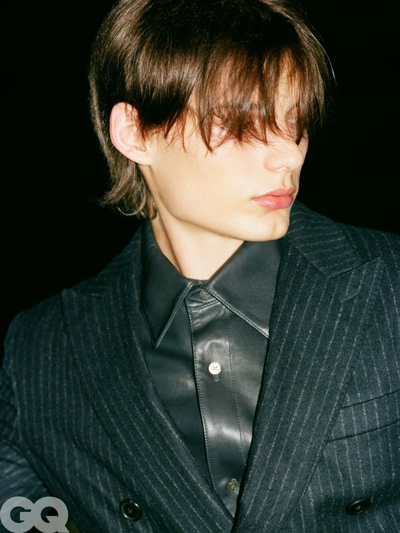 Model Meng Yu Qi wearing a pinstripe blazer over a black leather shirt against a black background.
