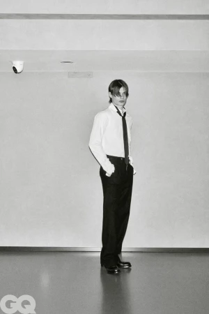 Male model Meng Yu Qi standing in a white collared shirt, black necktie, and dark trousers in a minimalist monochrome setting.