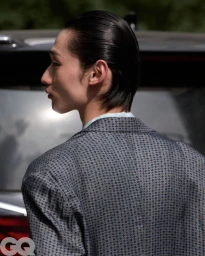 Profile view of model Chengwei Dong in a patterned grey blazer with slicked-back hair outdoors.