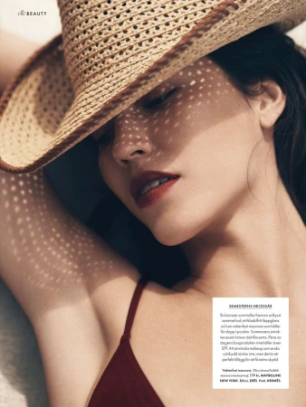 Woman wearing a straw hat in a close-up shot, casting dappled shadows across her face in a beauty advertisement with 'Elle Beauty' logo.