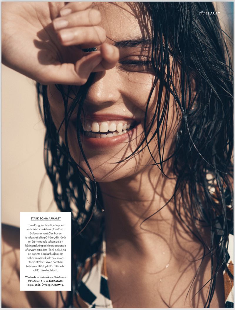 Close-up of a smiling woman with wet dark hair, shielding her eyes with her hand. Beauty and skincare advertising photography.