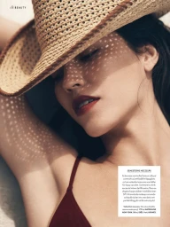 Close-up of a model wearing a woven straw hat casting dappled shadows across her face and dark red lipstick for Elle Sweden.