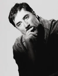 Black and white portrait of actor Javier Bardem resting his hand on his chin against a plain light studio backdrop.