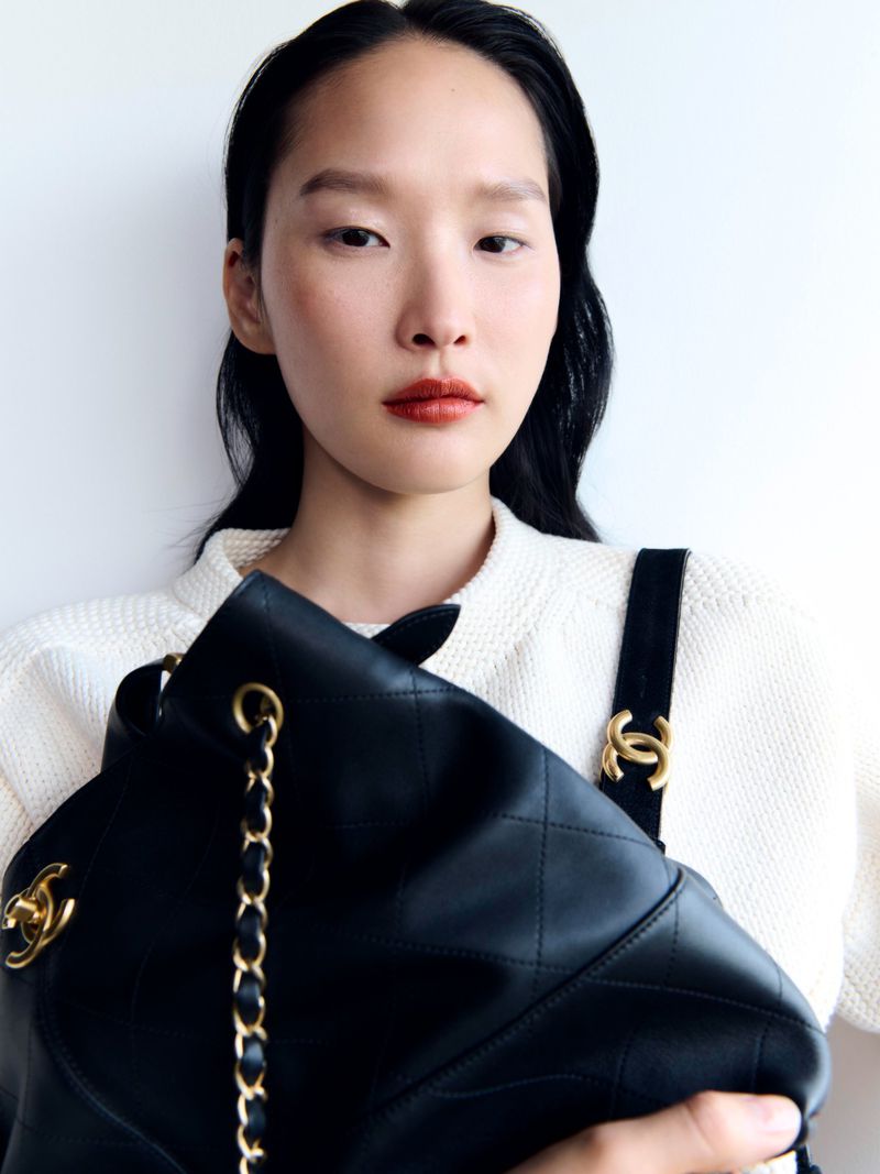 Close-up shot of an Asian female holding a black leather Chanel handbag against a white background. Focus on the bag and model.