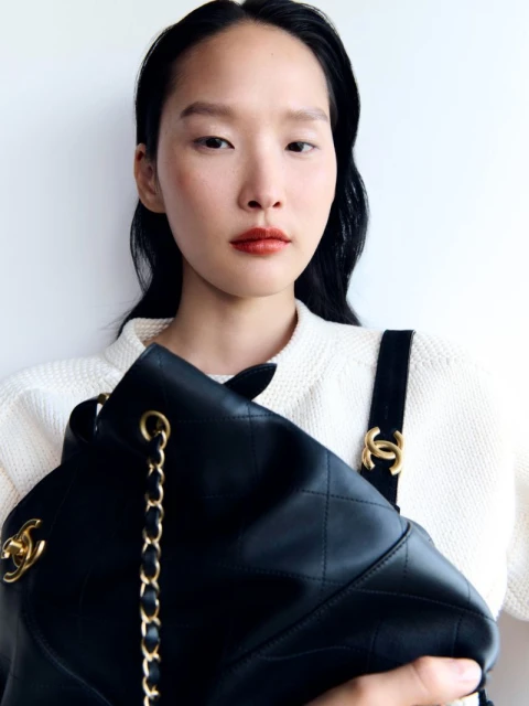 Close-up shot of an Asian female holding a black leather Chanel handbag against a white background. Focus on the bag and model.