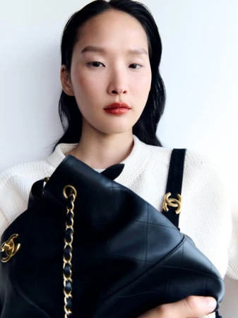 Close-up shot of an Asian female holding a black leather Chanel handbag against a white background. Focus on the bag and model.