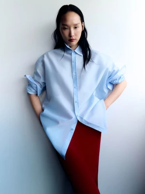 Model wearing a light blue button-up shirt and a long red skirt against a plain white studio background.