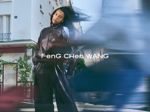 Model wearing a dark brown leather tracksuit standing on a city street with windblown hair and motion blur.