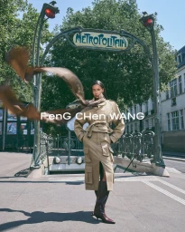 Model wearing a beige utilitarian trench ensemble and flowing brown scarf in front of an Art Nouveau Paris Metro entrance.