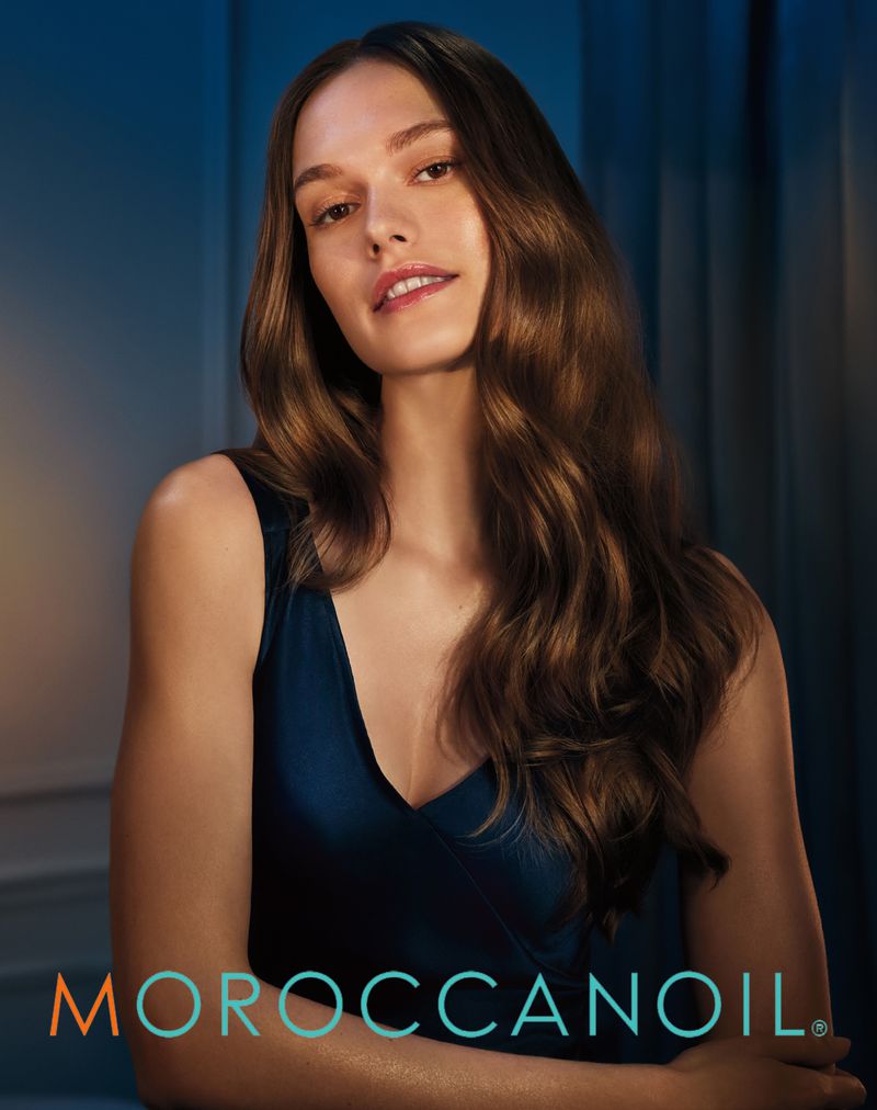 Model with long wavy brown hair wearing a dark blue v-neck top for Moroccanoil, photographed by Andrew Yee.