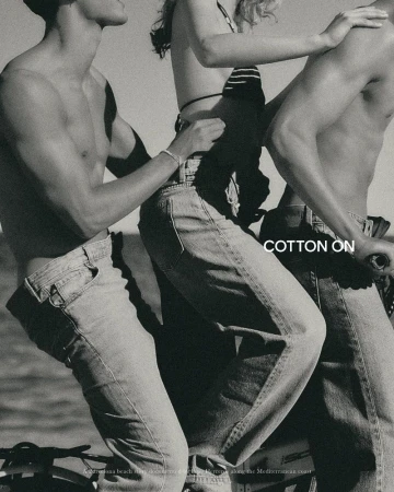 Black and white photo of three young adults in denim jeans riding together on a bicycle near the water for Cotton On.