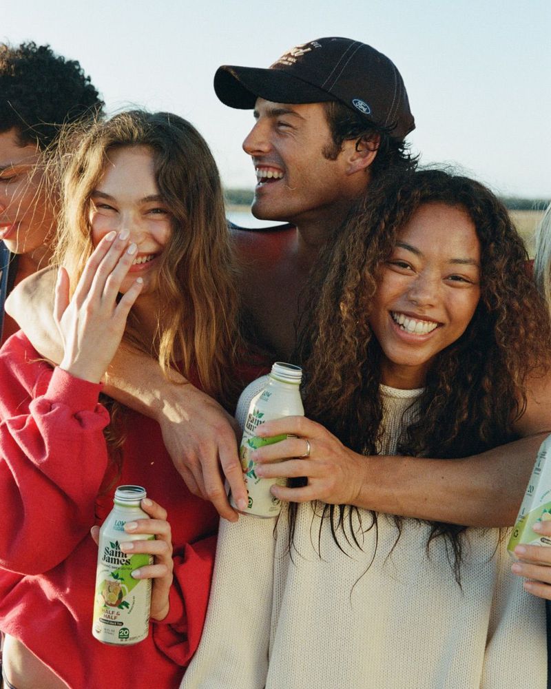 Group of smiling young friends outdoors holding bottles of Saint James iced tea in warm natural sunlight.