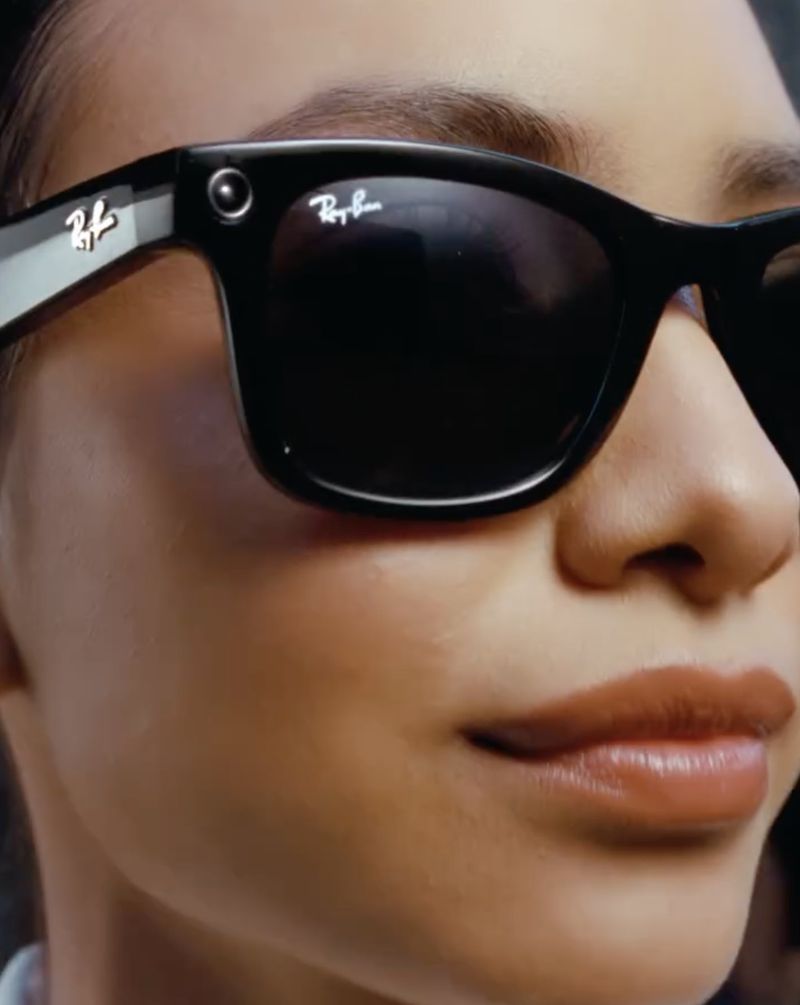 Extreme close-up of a woman wearing black Ray-Ban Meta smart sunglasses with dark tinted lenses and built-in camera.