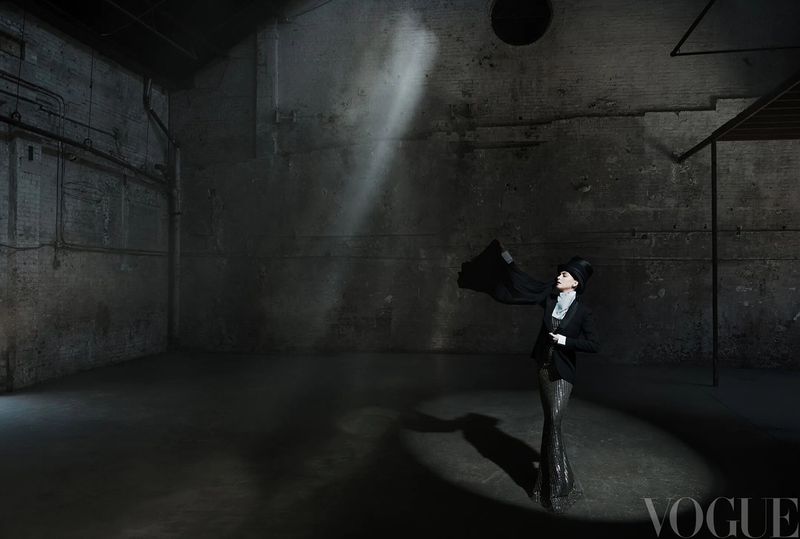 Anne Hathaway posing under a dramatic spotlight in a top hat and dark tailored jacket inside an industrial warehouse for Vogue China.
