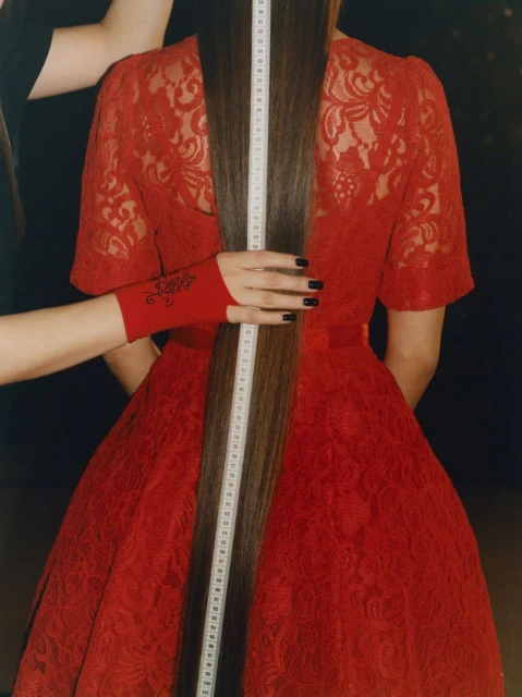 Back view of woman in red dress with extra-long straight hair being measured by hands with red sleeves and black manicure.