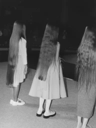 Three young girls with long hair wearing dresses seen from behind in a monochrome photograph