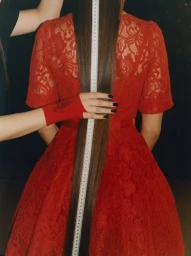 Rear view of a woman in a red lace dress with a measuring tape held down her long brown hair by Francesca Allen for Plaukai.