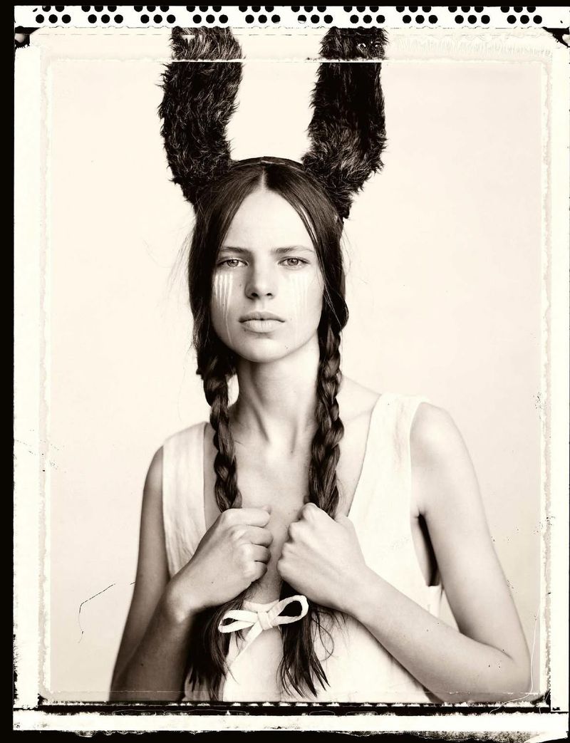 Model Valerie Margareta wearing dark fuzzy ears and holding braided pigtails in a black and white studio portrait.