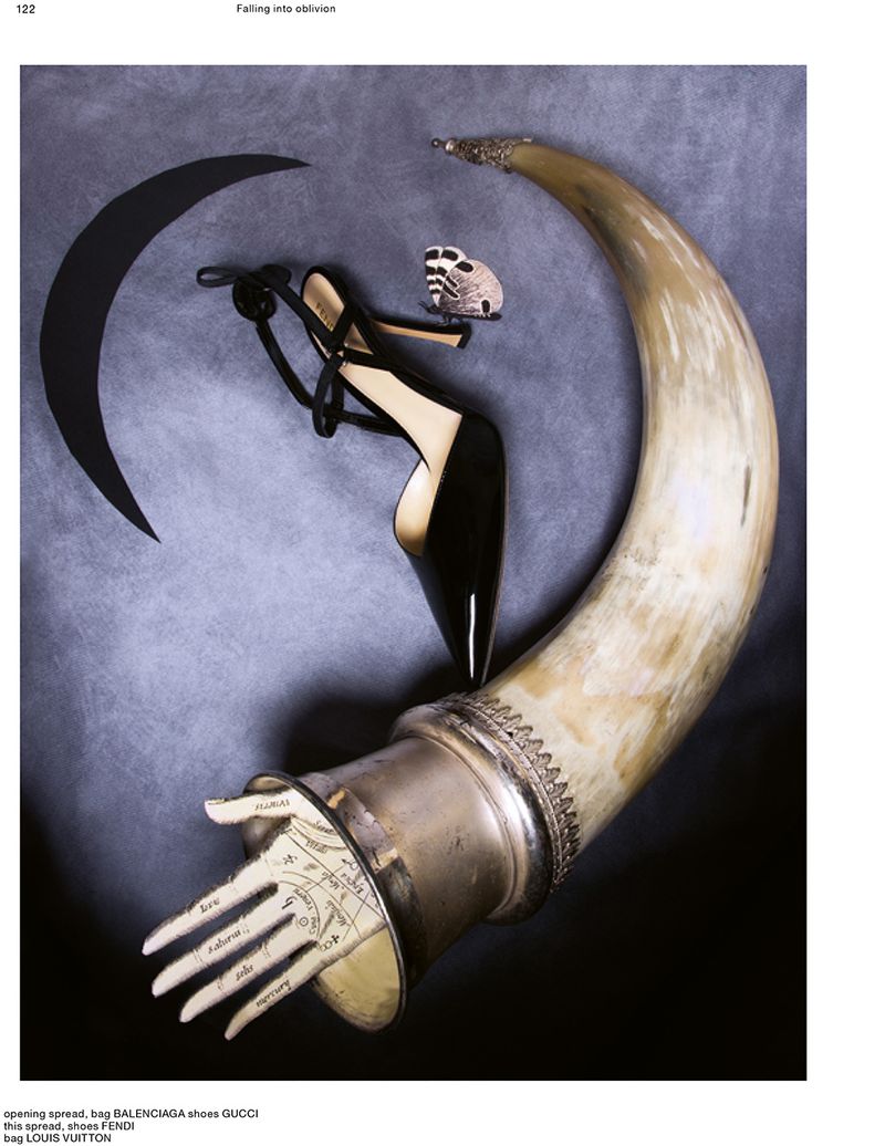 Surreal fashion still life with a black pointed-toe stiletto pump, a large horn with a palmistry hand, and a moth against grey backdrop.