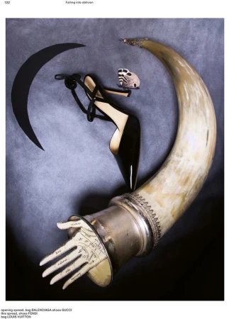 Surreal fashion still life with a black pointed-toe stiletto pump, a large horn with a palmistry hand, and a moth against grey backdrop.