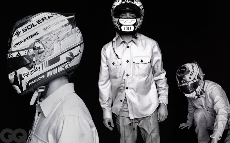 Black and white editorial photo of driver Kimi Antonelli wearing a racing helmet and buttoned overshirt against a black background.