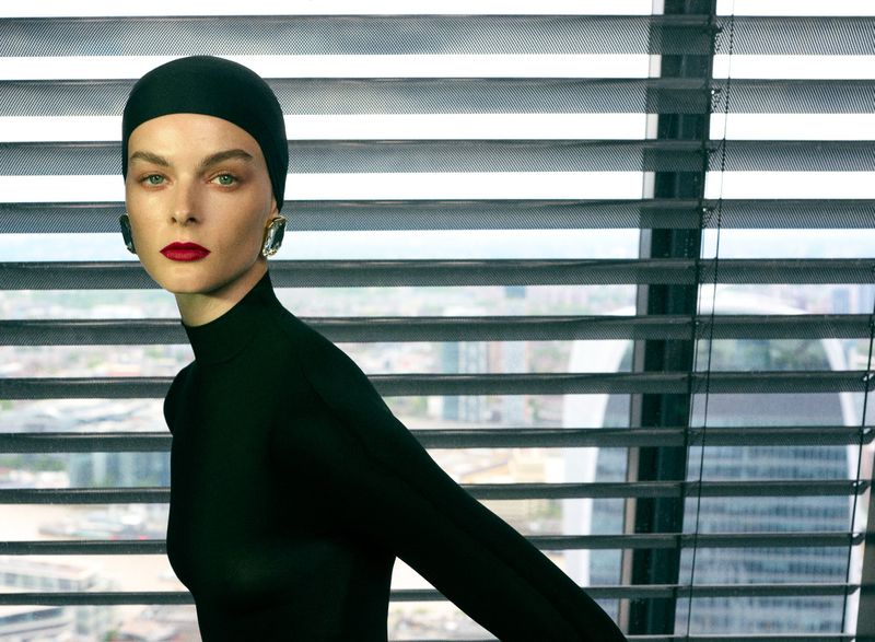 Aylah Peterson wearing a black head cap and high-neck top with bold red lipstick posed in front of window blinds.