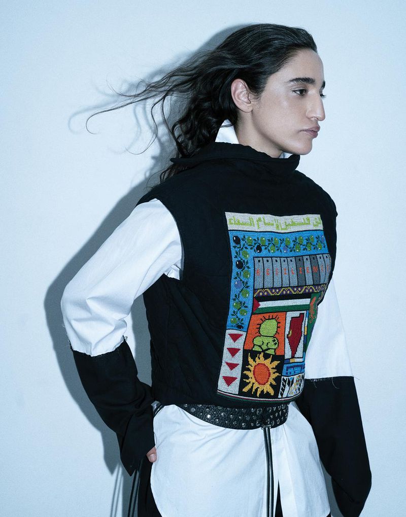 Palestinian DJ Sama' Abdulhadi wearing a black graphic vest over a white collared shirt against a white backdrop.