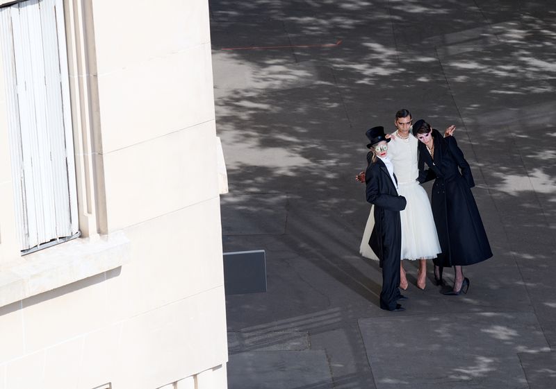 Three models in avant-garde black and white fashion posing on an outdoor paved ground seen from a high camera angle.
