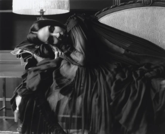 Black and white portrait of Tish Weinstock reclining on an ornate antique chaise lounge beneath a fringed lamp.