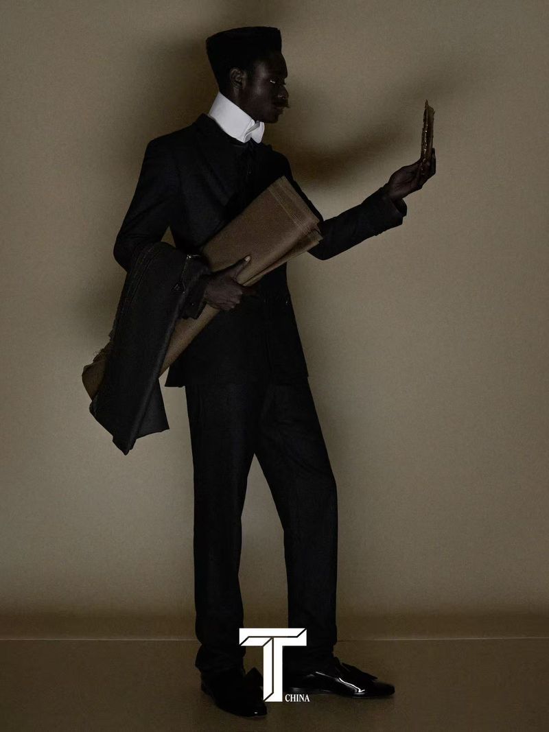 Rodney Osei wearing a dark tailored suit and high white collar holding fabric against a neutral studio backdrop.