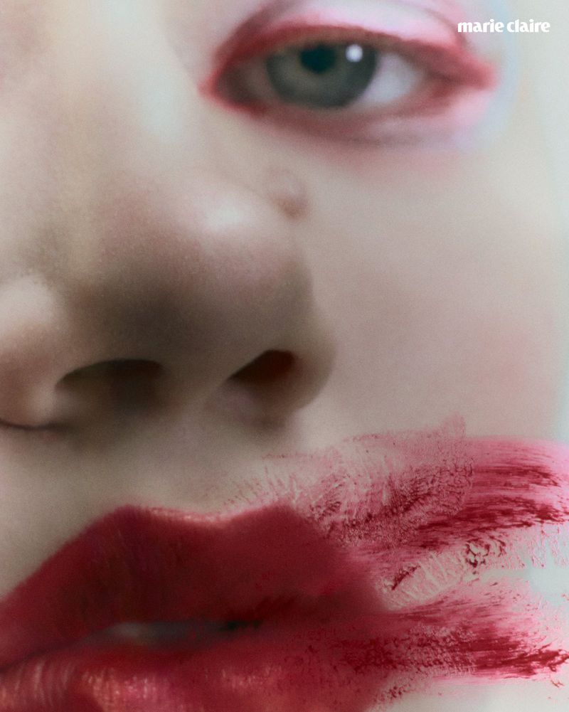 Extreme close-up beauty portrait featuring smeared red lipstick and soft pink eye makeup on pale skin.