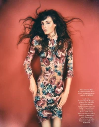 Model Matilde de Nard lying against a warm red backdrop wearing a long-sleeved floral printed dress with hair spreading outwards.