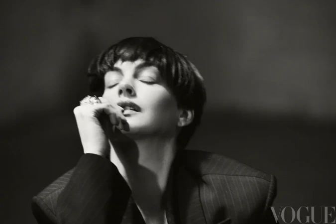 Black and white portrait of Anne Hathaway with short dark hair wearing a pinstripe blazer with her hand raised near her lips.