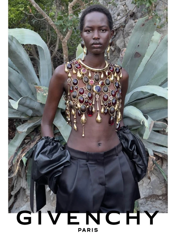 Model Nyaduola Gabriel wearing elaborate jewel-encrusted harness and black trousers outdoors for Givenchy