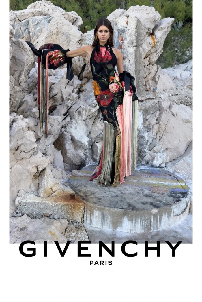 Model Kaia Gerber wearing a floral halter dress posing against rocky terrain for Givenchy