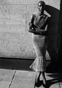 Black and white portrait of a model leaning against a textured stone wall wearing a sleeveless fringe dress.