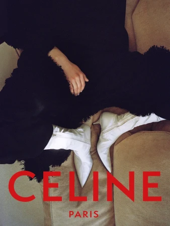 Person wearing pointed-toe white heeled ankle boots and a textured black garment on a sofa with red Celine Paris typography.