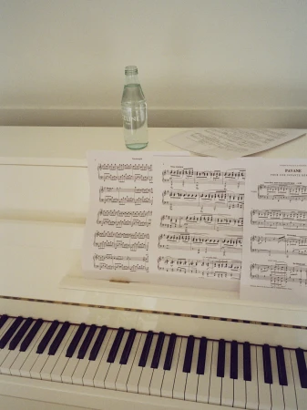 White upright piano with classical sheet music on the stand and a clear branded water bottle resting on top.