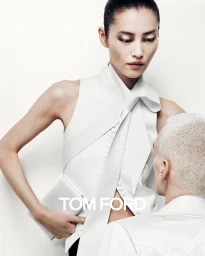 Model Liu Wen in a structured white sleeveless top holding a white clutch, standing next to a man against a plain background