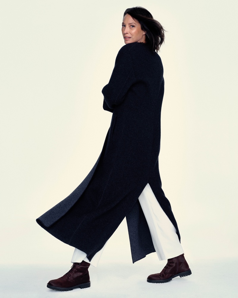 Christy Turlington wearing a long dark coat and white trousers against a pale background
